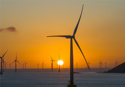 An offshore wind farm in front of an orange sky. 