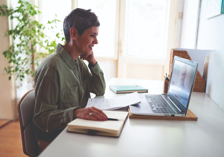 A woman in a green top sits at a laptop in a bright room. 