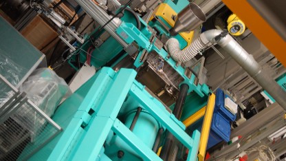 Polymer processing machine in a factory, featuring blue and yellow pipes for injection moulding of polymers.