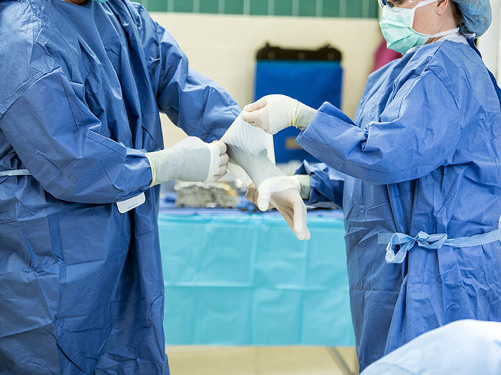 Two medical personnel standing in personal protective equipment in a medical room, while one of the people put gloves on the other